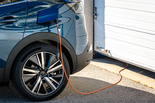 a blue electric car charges outside a garage
