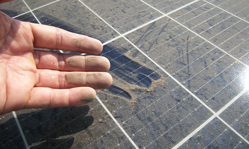 a man smears his fingers across a solar panel to dislodge dust