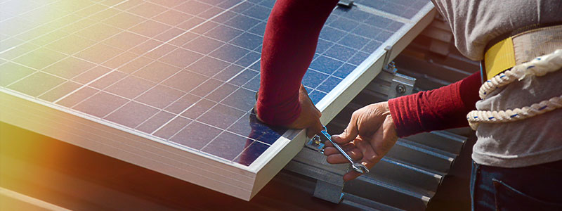 a roofer installs solar panels on a tin roof