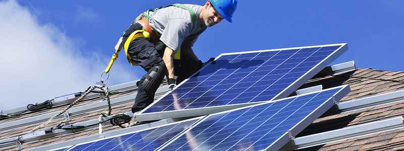 a professional roofer installs solar panels on a shingle roof